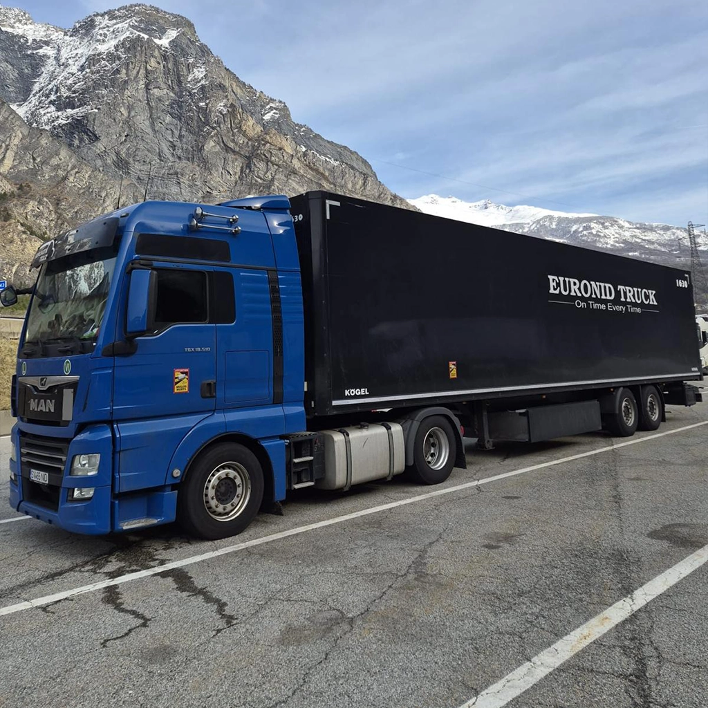 Camion MAN albastru si semiremorca tip box inscriptionata cu numele și sloganul companiei
